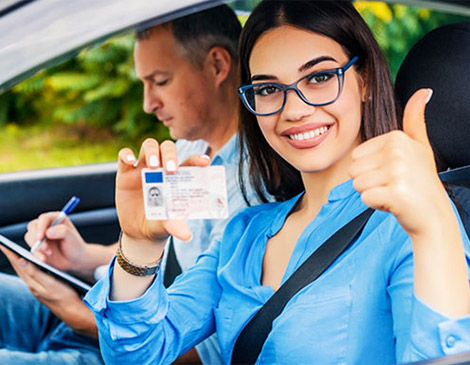 A woman holding up her driver 's license while sitting in the passenger seat of a car.