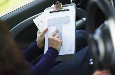 A person holding papers in their hand while sitting in the driver 's seat of a car.